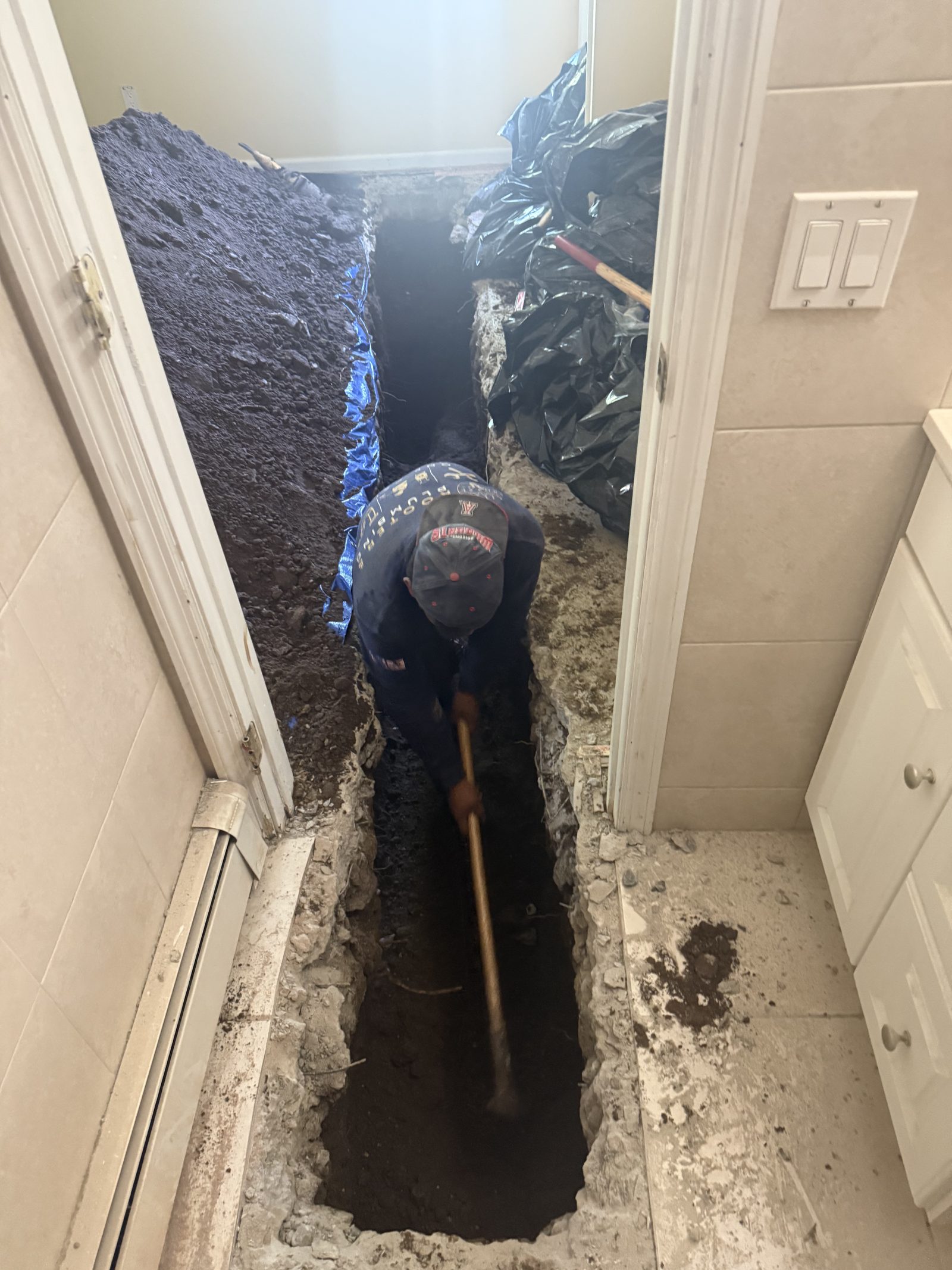 Heights plumber excavating a trench for an under-slab drain line inside a New Jersey home