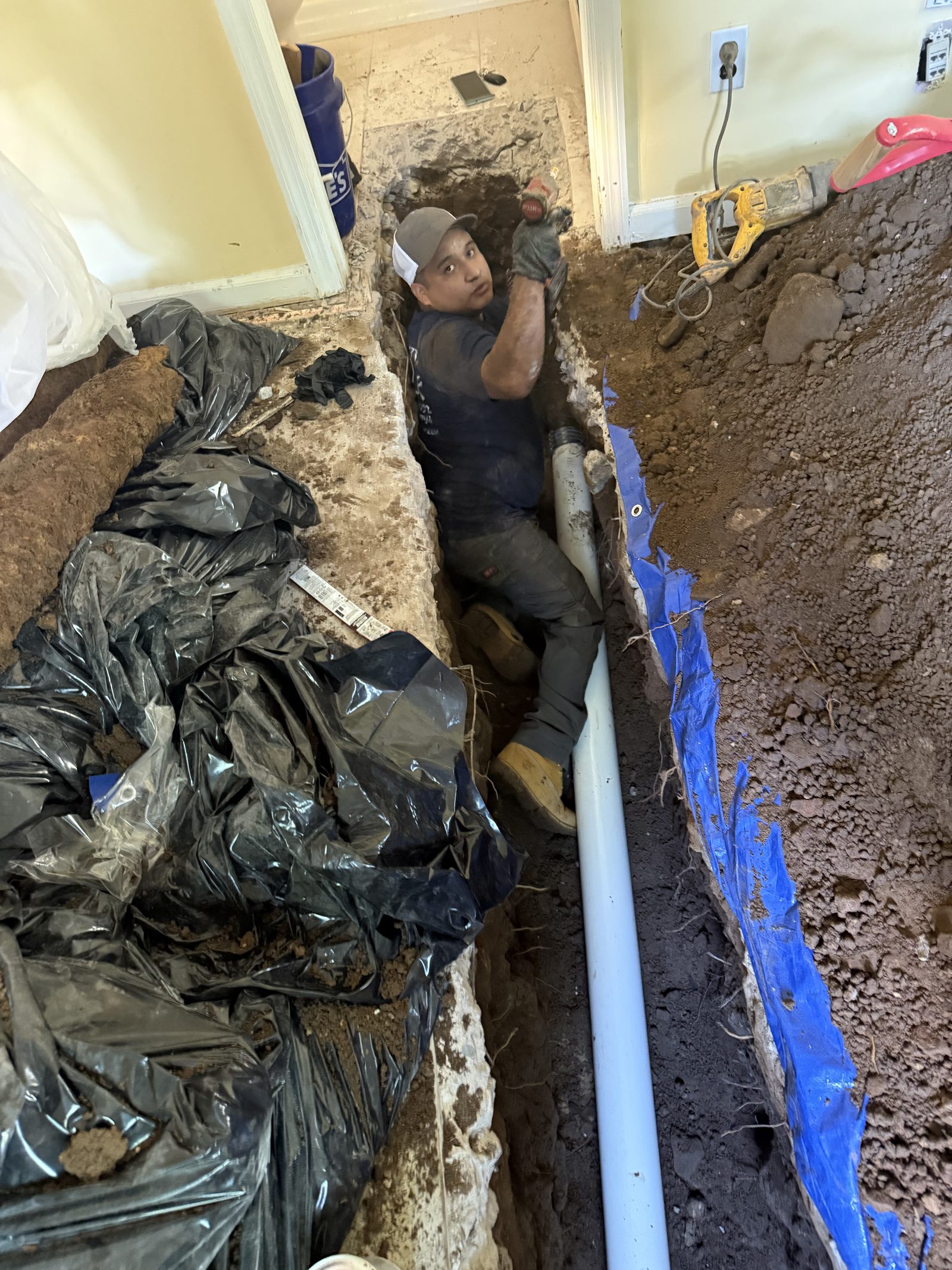 Heights plumber laying a new PVC drain line in a trench cut through a New Jersey basement slab