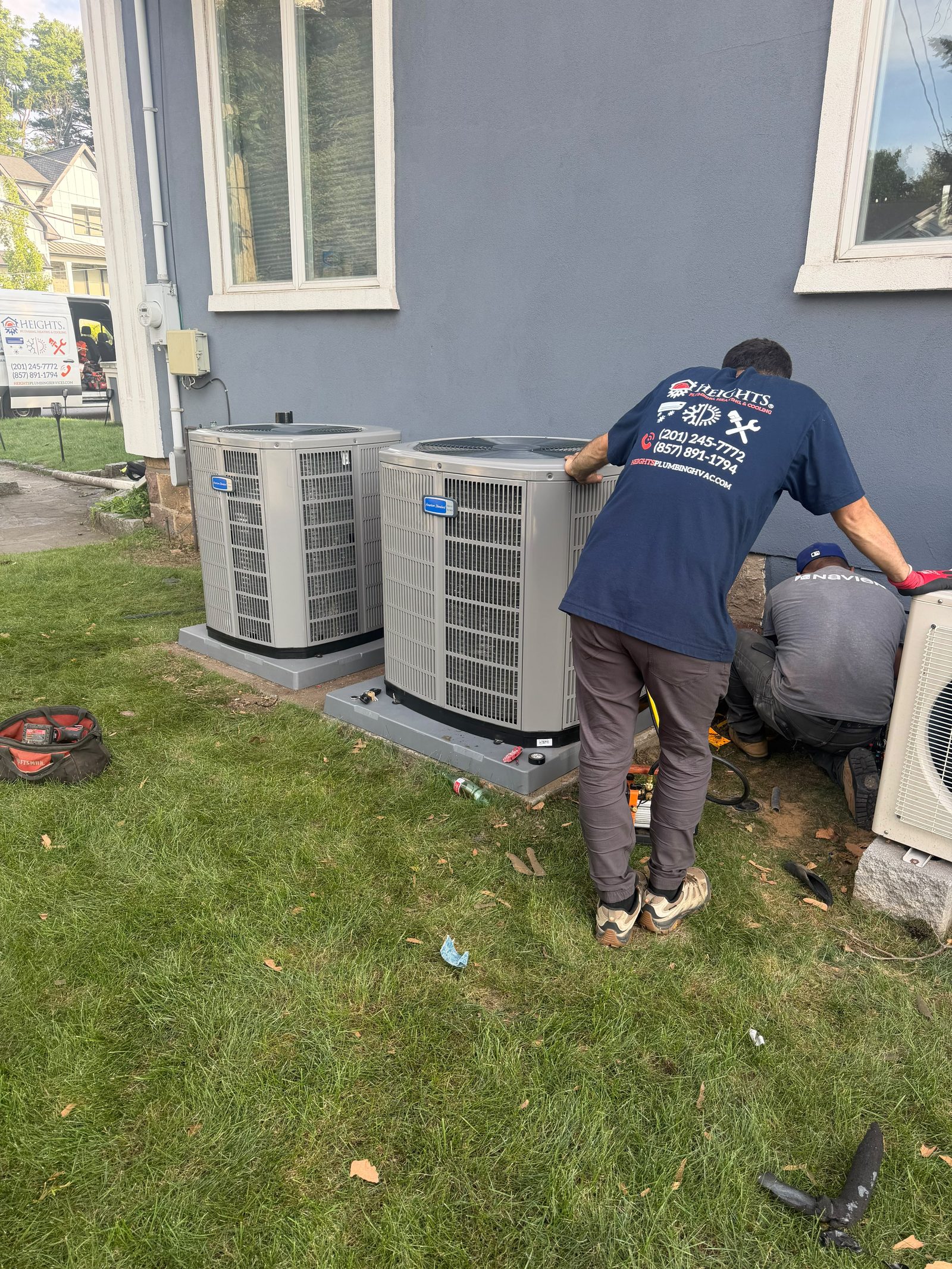 Two Heights technicians servicing central air condensers behind a New Jersey home