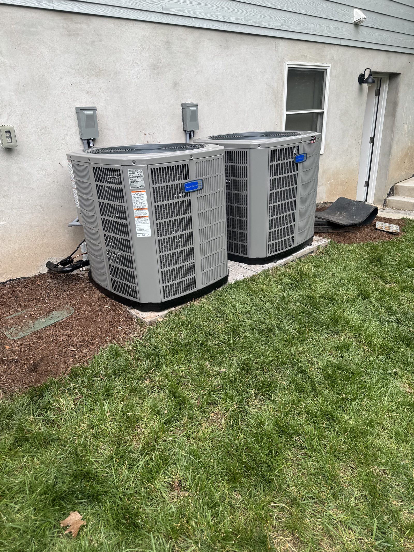Two new central air conditioner condensers installed on pads beside a New Jersey home